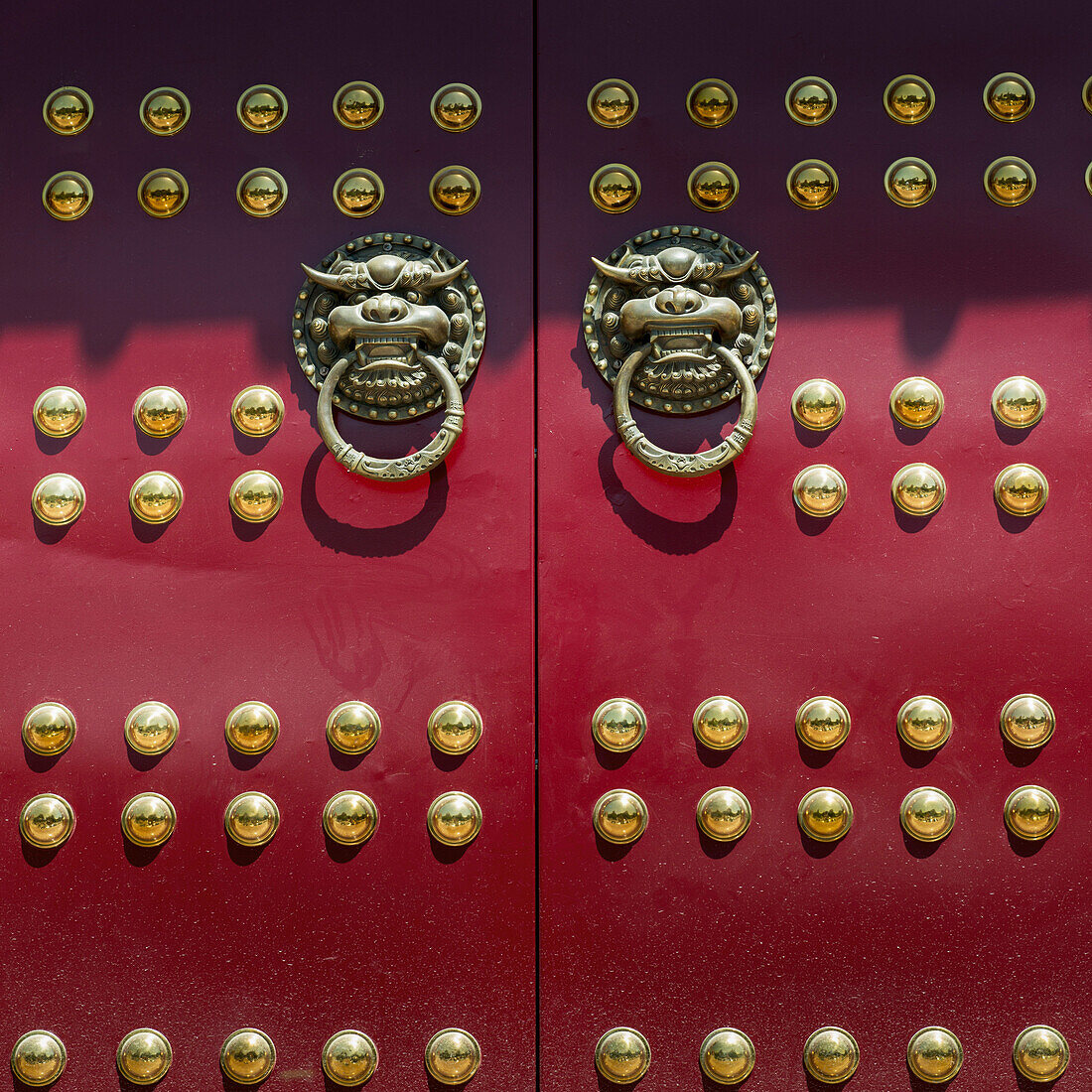 Red doors with round gold decorative pieces and door knockers in animal likeness
