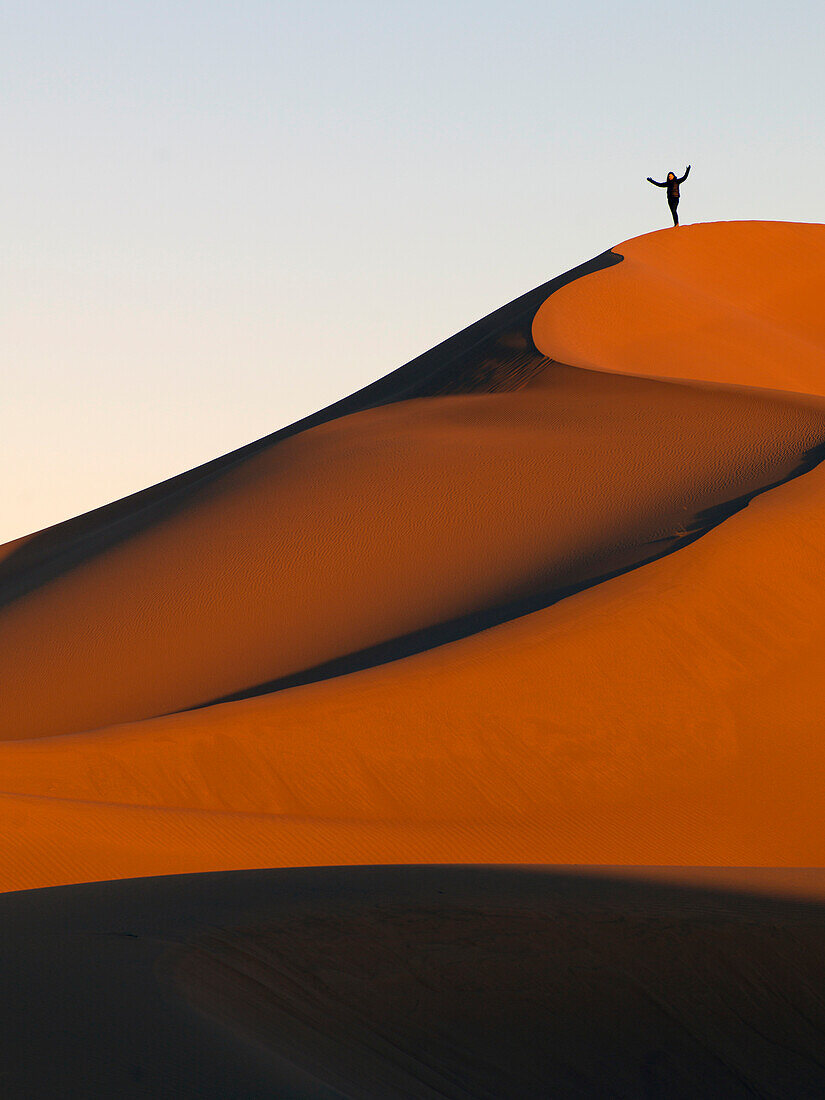 A person stands on a top ridge of a sand slope