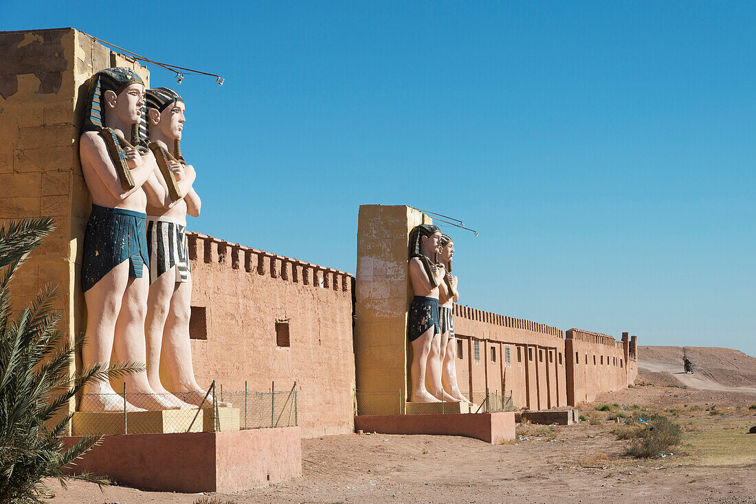 Statues of Egyptian male figures along a wall and a blue sky