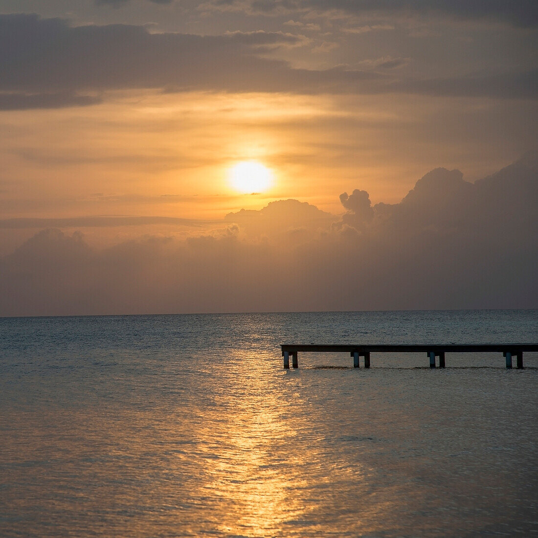 'Silhouette Of A Dock Leading Out To Water With The Sun Setting In A Dramatic Sky; Utila, Bay Islands, Honduras'