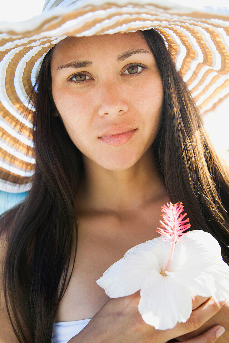 'Portrait Of A Young Woman In A Sunhat Holding An Hibiscus Flower, Waikiki, Oahu, Hawaii, United States Of America'