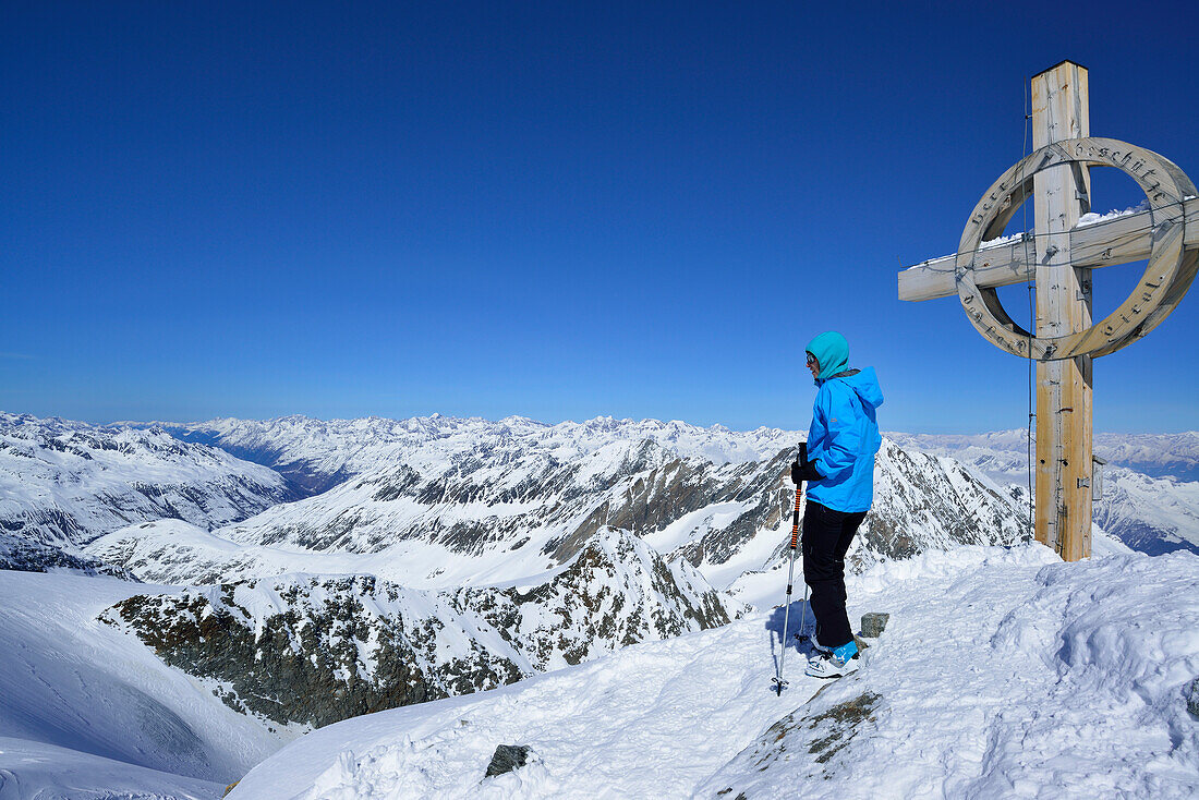 Female back-country skier standing beside a summit cross, Hinterer Seelenkogel, Obergurgl, Oetztal Alps, Tyrol, Austria