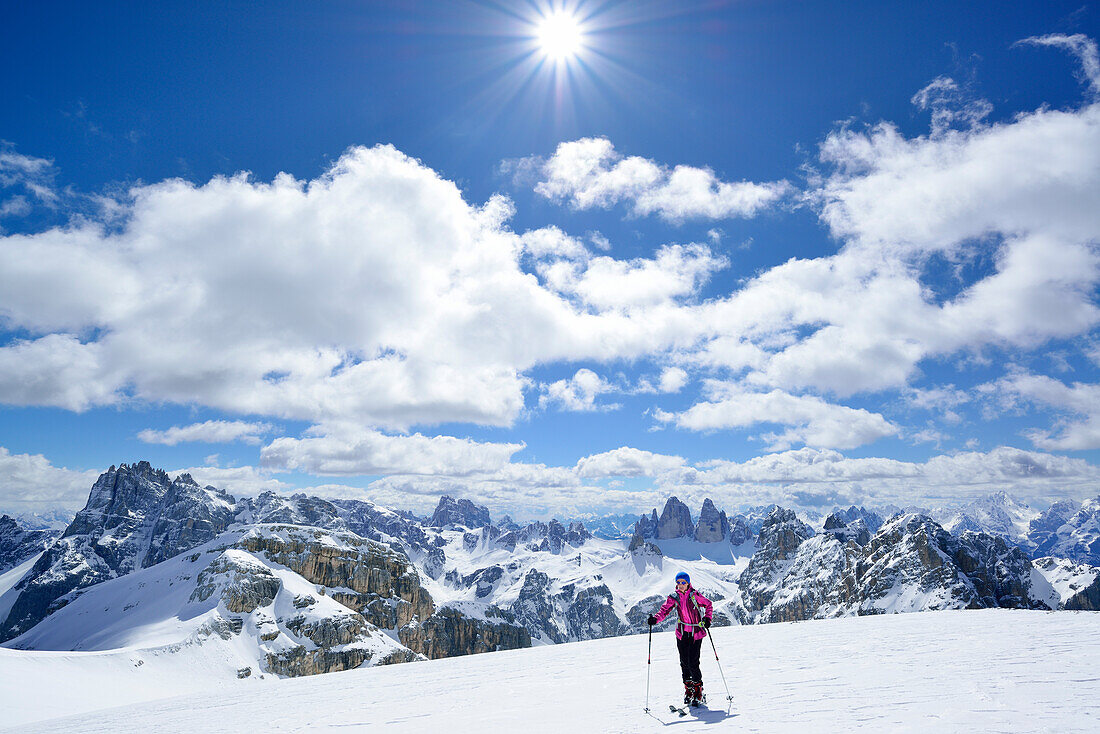 Frau auf Skitour steigt zum Hochebenkofel auf, Dreischusterspitze, Zwölferkofel, Drei Zinnen und Schwalbenkofel im Hintergrund, Sextener Dolomiten, Südtirol, Italien