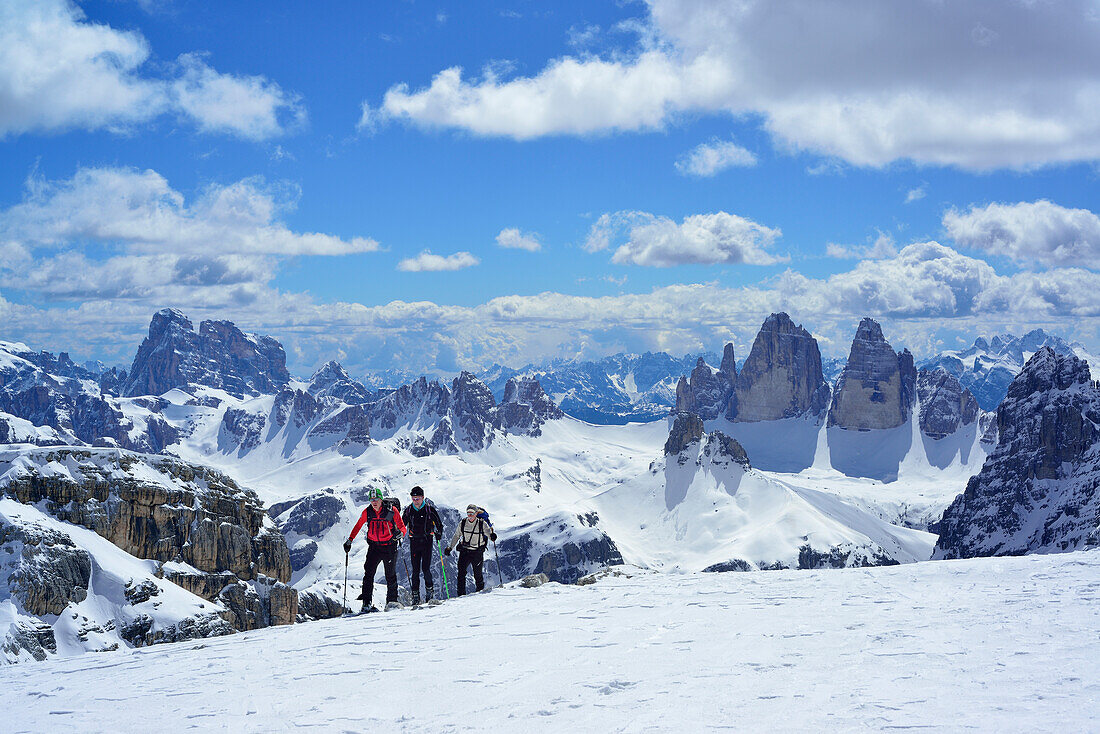 Skitourengeher steigen zum Hochebenkofel auf, Zwölferkofel und Drei Zinnen im Hintergrund, Sextener Dolomiten, Südtirol, Italien