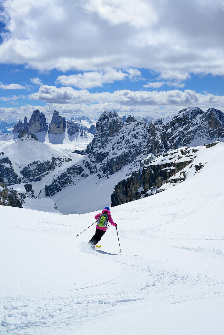 Frau auf Skitour fährt vom Hochebenkofel ab, Drei Zinnen im Hintergrund, Sextener Dolomiten, Südtirol, Italien