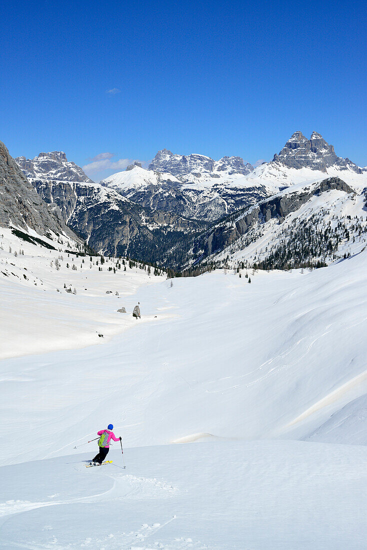 Frau auf Skitour fährt vom Corno d'Angolo ab, Drei Zinnen im Hintergrund, Cristallo, Dolomiten, Venetien, Italien
