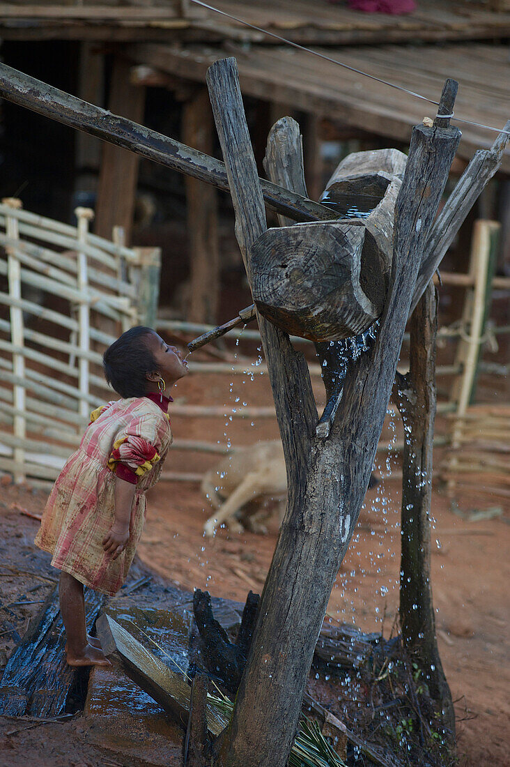 Mädchen trinkt am Abend aus einem hölzernen Wasserspender, Eng, Ann Dorf bei Kyaing Tong, Kentung, Shan Staat, Myanmar, Burma