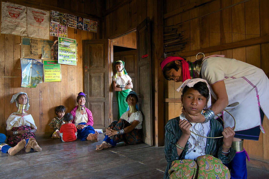 Langhals Frauen mit typischem Halsschmuck, eine 13-jährige Schülerin bekommt auf eigenen Wunsch zum ersten Mal den Halsschmuck angelegt, Padaung Frauen in ihrem Haus bei Loikaw, Kayah Staat, Karenni Staat, Myanmar, Burma, Asien