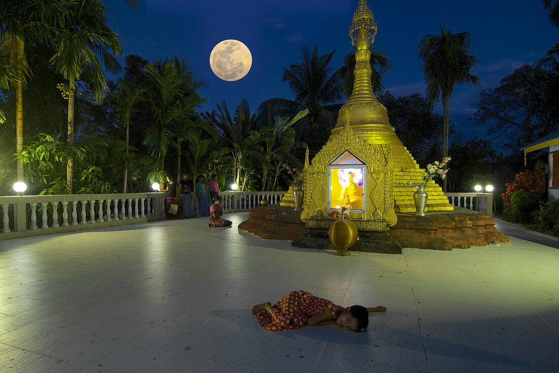 Child lying on the floor in front of a small pagoda in Lonthar village, Ngapali, most famous beach resort in Burma at the Bay of Bengal, Rakhaing State, Arakan, Myanmar, Burma