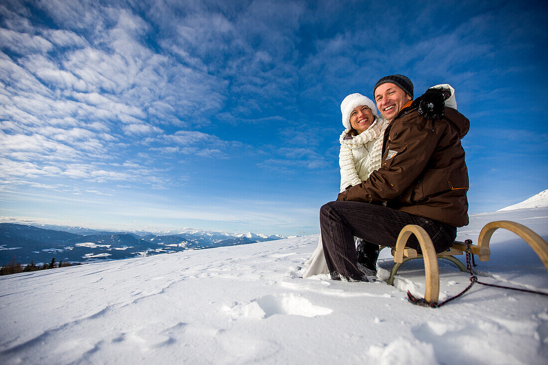 Paar sitzt auf einem Schlitten in Schnee, Mühlen, Steiermark, Österreich