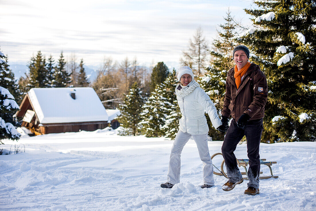 Paar mit einem Schlitten spaziert im Schnee, Mühlen, Steiermark, Österreich