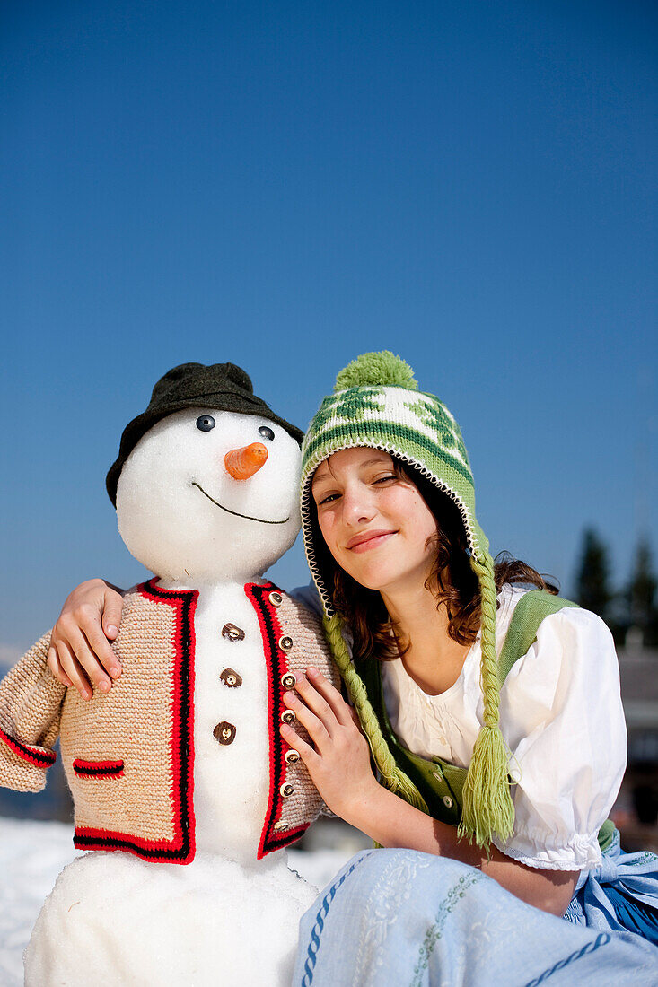 Mädchen im Dirndl neben einem Schneemann, Frauenalpe, Murau, Steiermark, Österreich
