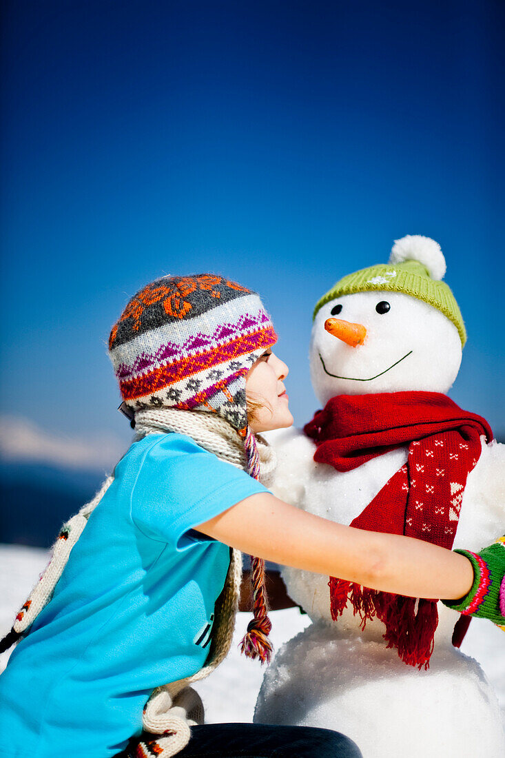 Mädchen umarmt einen Schneemann im Fühling, Frauenalpe, Murau, Steiermark, Österreich