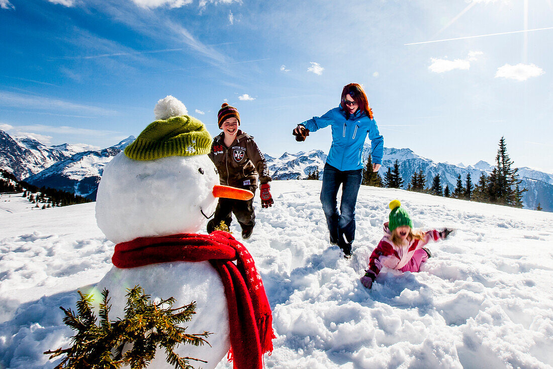 Mutter mit zwei Kindern im Schnee bei einem Schneemann, Planai, Schladming, Steiermark, Österreich