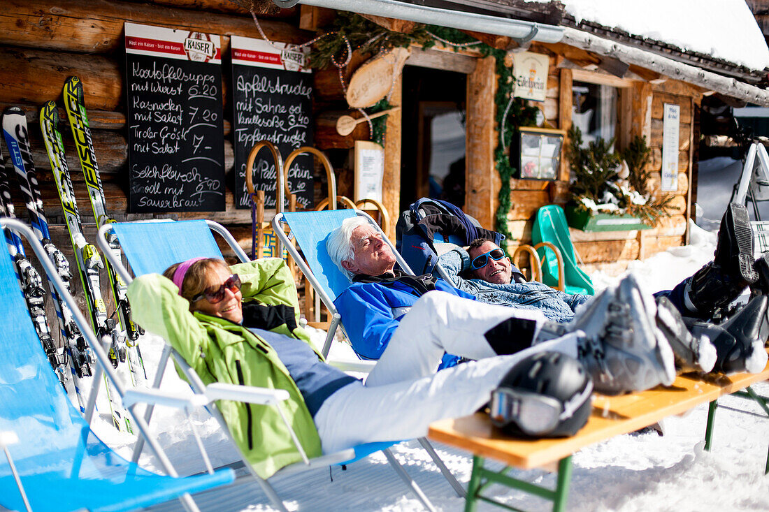 Three skiers sunbathing in front of a ski lodge, Fageralm, Salzburg, Austria