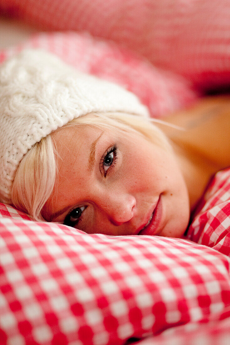 Junge Frau mit Mütze liegt im Bett