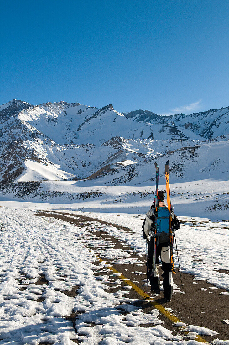 Skifahrer läuft verschneite Straße entlang, schneebedeckte Berge im Hintergrund, Las Lenas, Mendoza, Argentinien