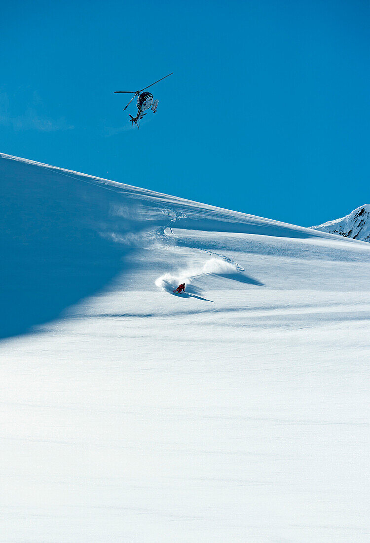Skier downhill skiing in deep snow, helicopter in background, Chugach Powder Guides, Girdwood, Alaska, USA