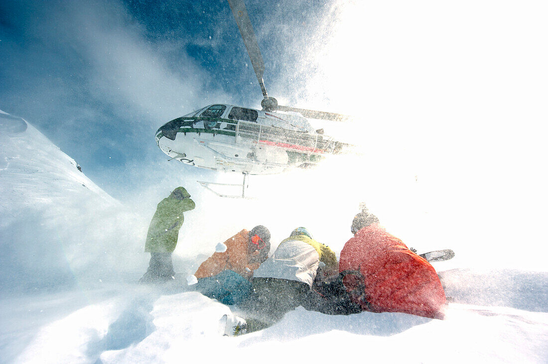 Skifahrer kauern im Rotorwind nach Ausstieg beim Heliskiing, Chugach Powder Guides, Girdwood, Alaska, USA