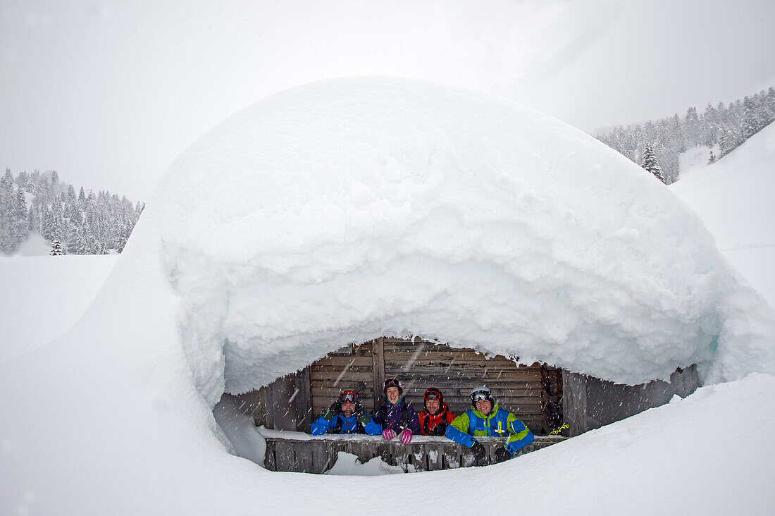 Four skiers in front of a snow-covered cabin, Corvara, South Tyrol, Italy