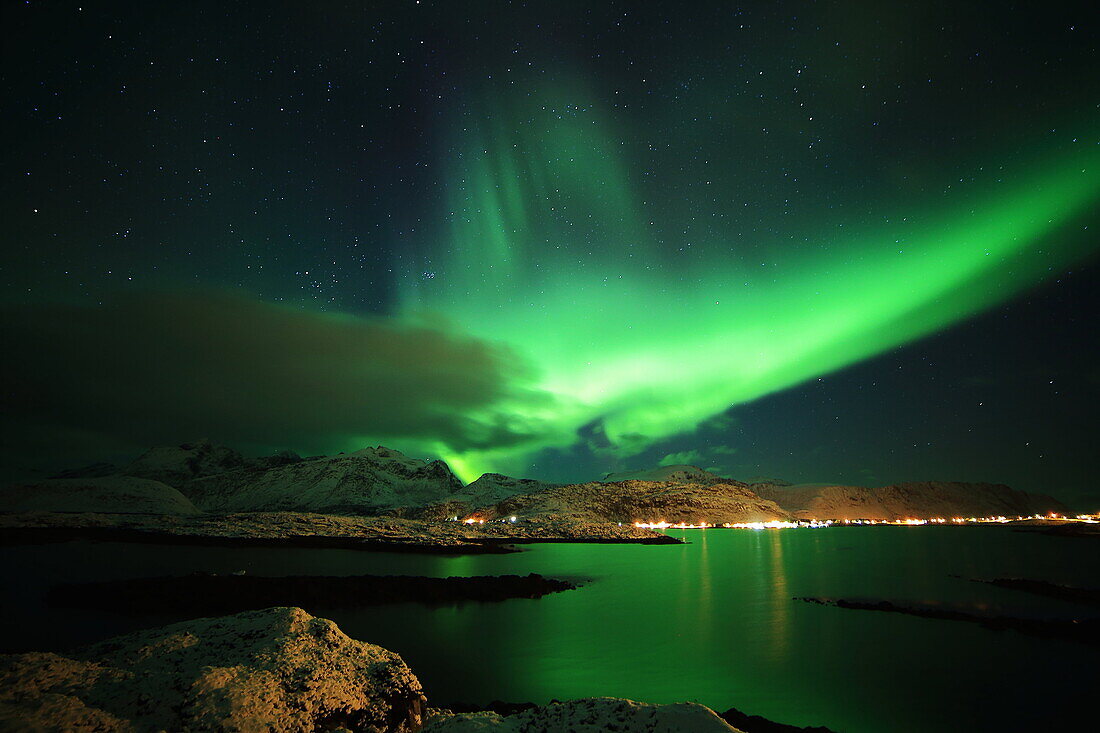 Green aurora borealis reflected in the fiord with the light town's and big mountains