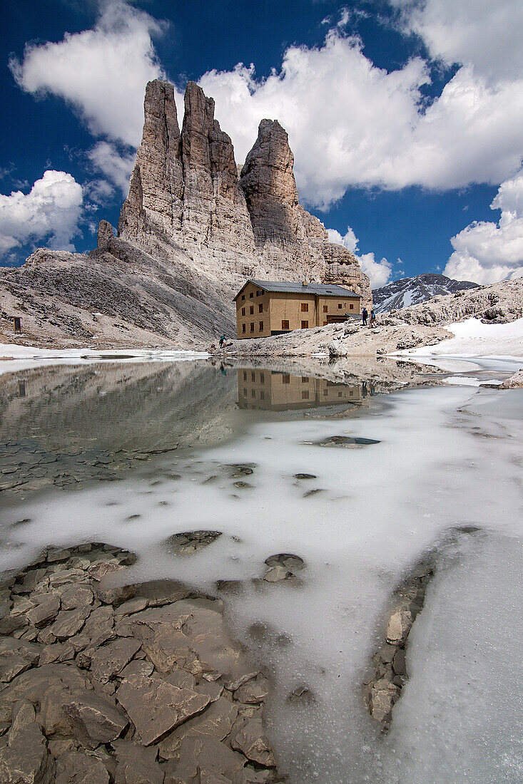 Little alpine lake, in the beginning of summertime, with a refuge and wonderful towers of dolomite, Dolomites