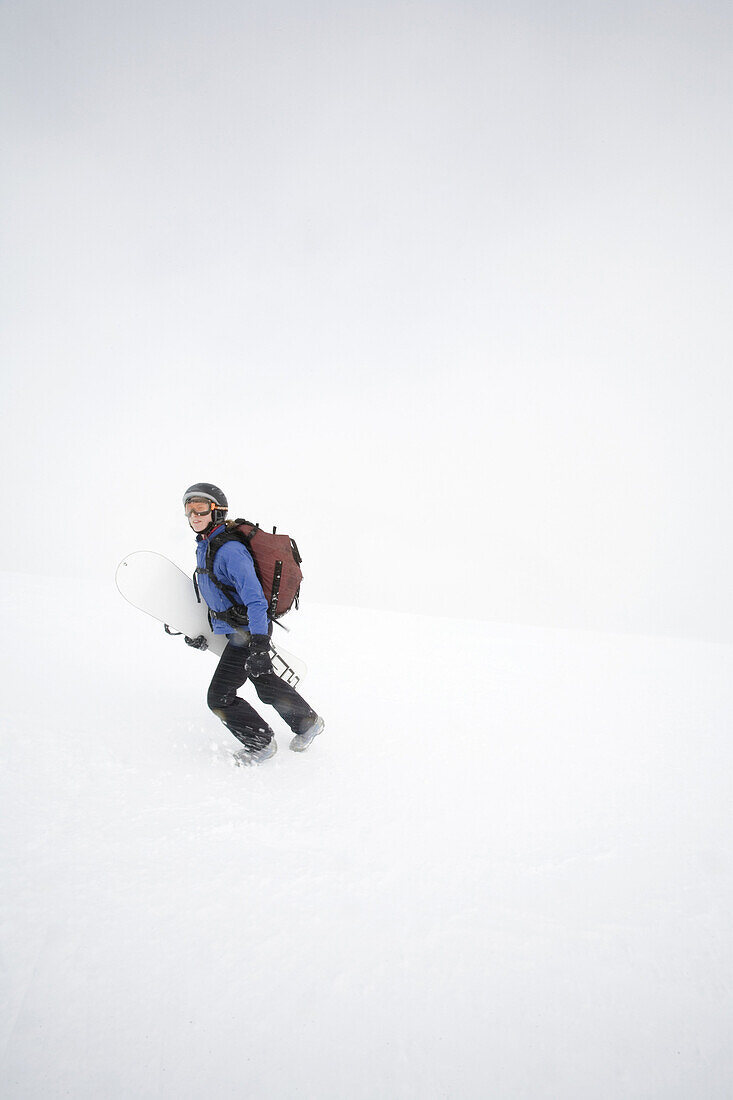 Young woman, Jess Meiris, carries snowboard under arm while hiking up Mt. Hood in the Oregon Cascades.