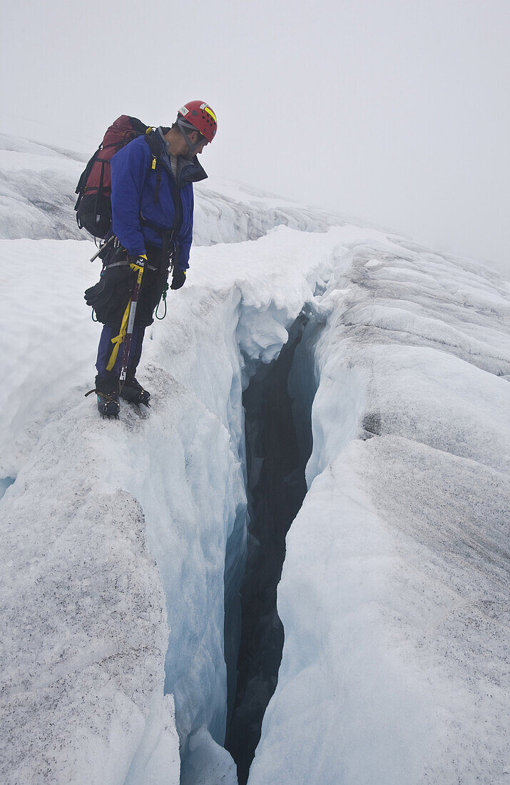 An mountaineer looks into a deep blue glacier crevasse.. Denver Glacier