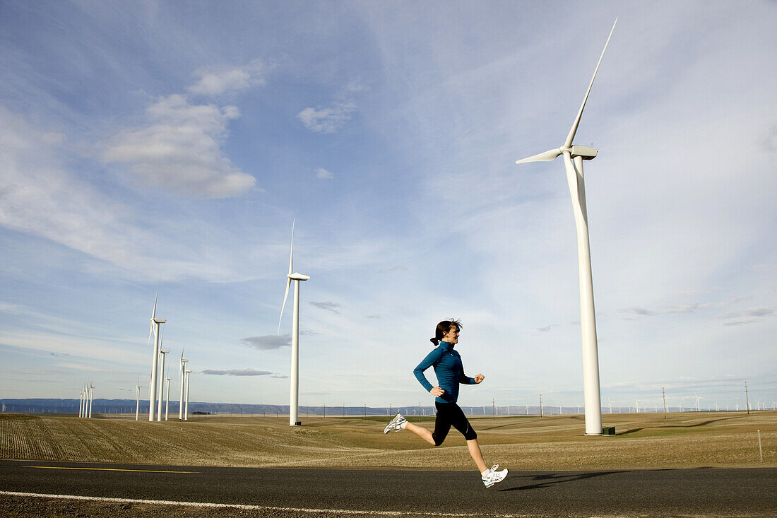A woman jogs a country road that passes through farmland scattered with windmills in the Columbia River Gorge, Oregon.