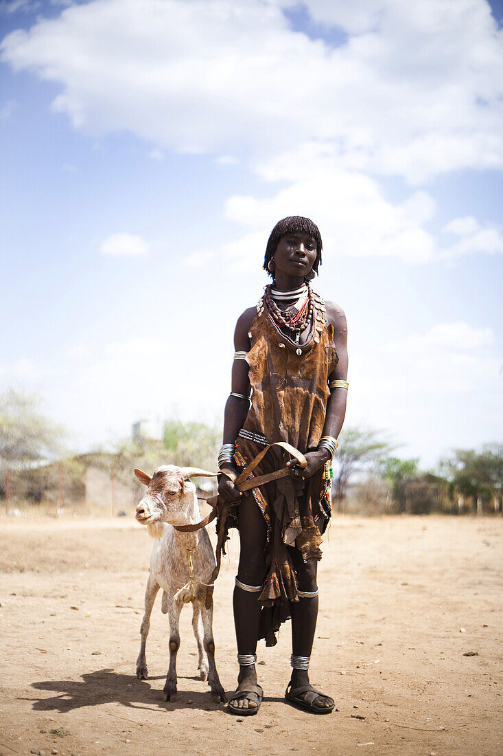 HAMER VILLAGE, OMO VALLEY, ETHIOPIA. A portrait of a woman standing next to her goat. She is dressed in traditional clothes of the Hamer people.