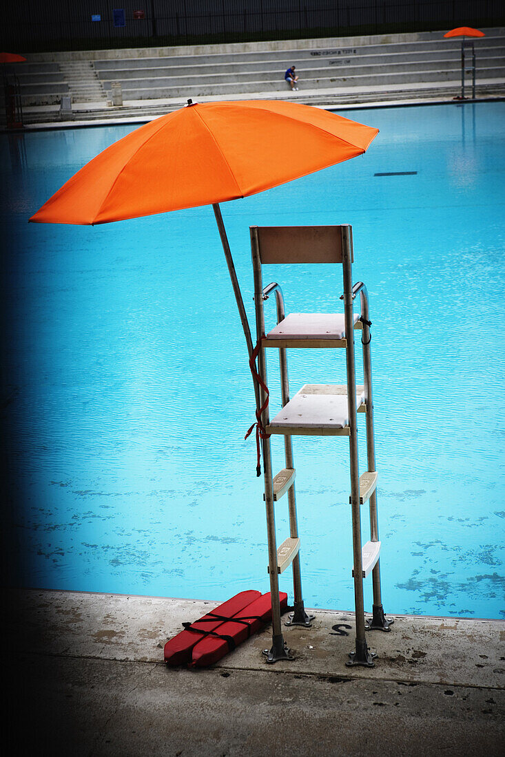 Orange umbrella on top a lifeguards stand overlooking a swimming pool in Central Park, Manhattan, New York City, New York.