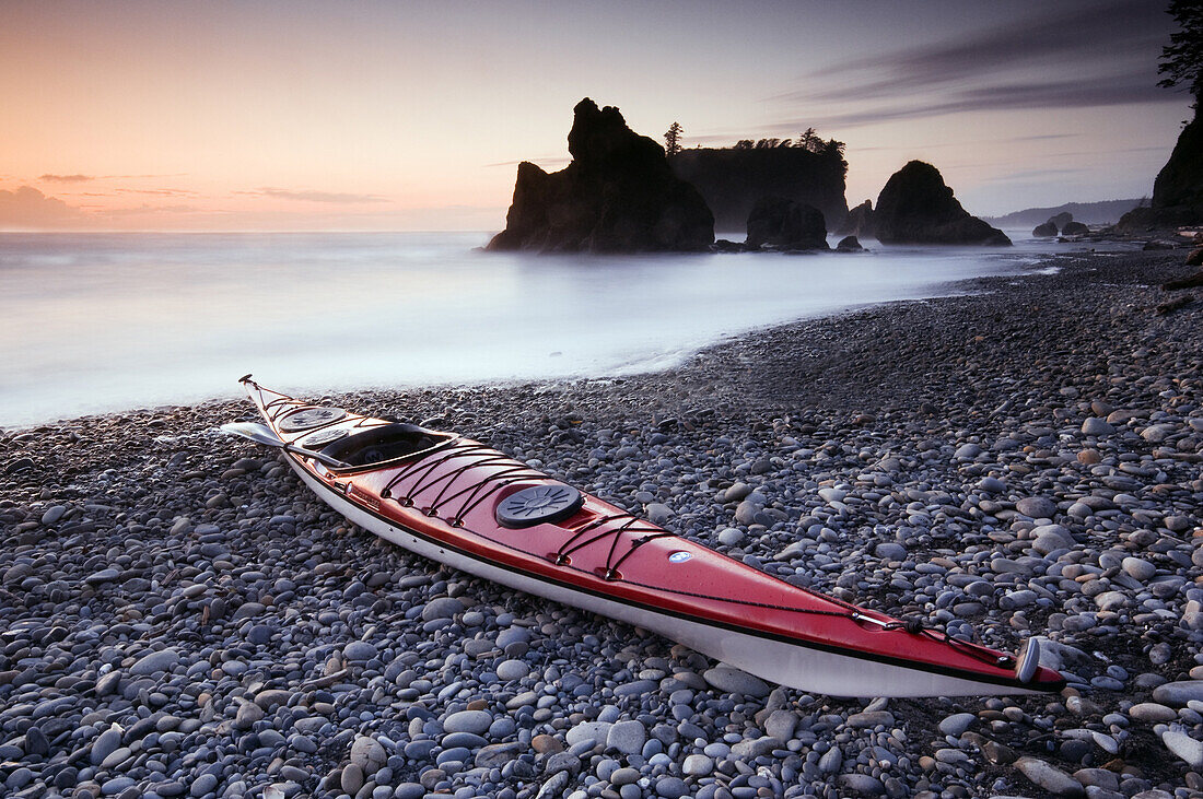 Red sea kayak lying on a pebble beach as the setting sun silhouettes sea stacks on the horizon, Ruby Beach, Olympic National Park, Washington, USA, 7 October 2008