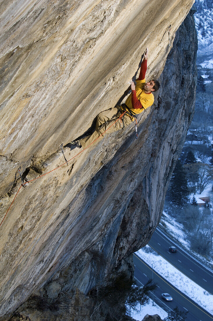 A rock climber in a yellow and red shirt reaching up for a hand hold on a steep and difficult route near Glenwood Springs Colorado.The climber is highlighted in light and the surrounding image is in blue shade.
