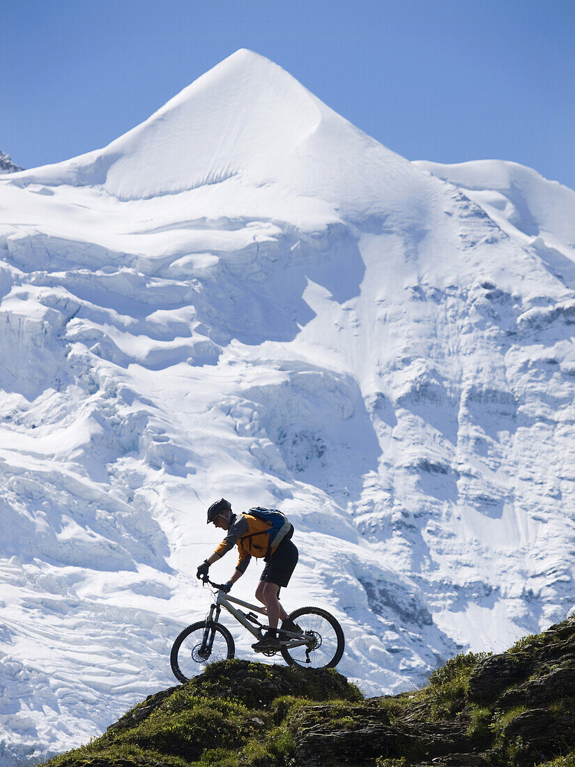 A mountain biker is balancing his bike on a steep slope near Kleine Scheidegg, above Grindelwald. In the background the Silberhorn mountain.