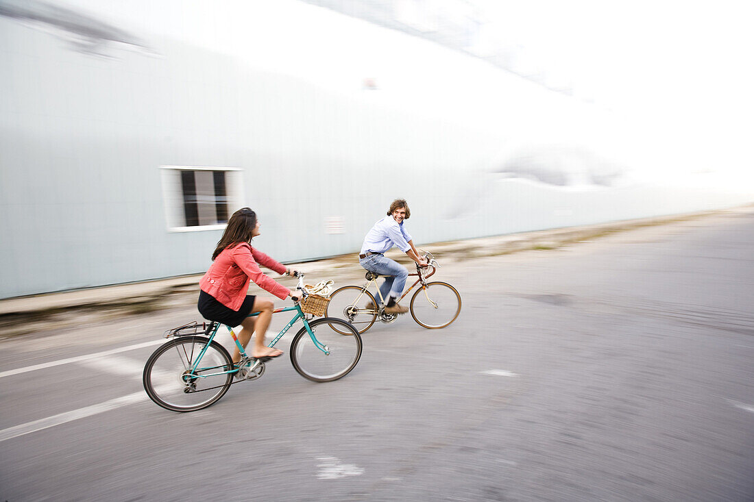 A smiling man and woman ride their bikes through a street in Portland, ME.