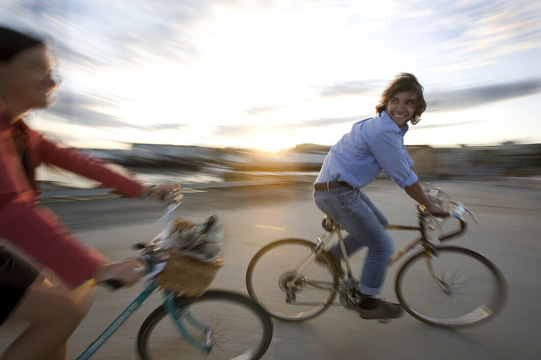 A young man and woman smile as they enjoy a sunny afternoon bike ride through an open street in Portland, ME. Motion Blur