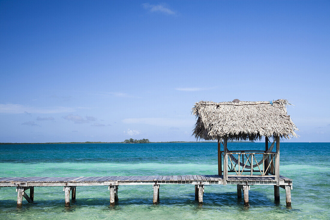 THATCH CAYE, BELIZE. A scenic image of a boardwalk, hammock and the crystal clear blue, green waters of the Caribbean.
