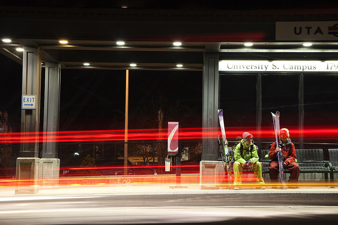 Two men wait for public transportation in Salt Lake City after a day of skiing, Utah.