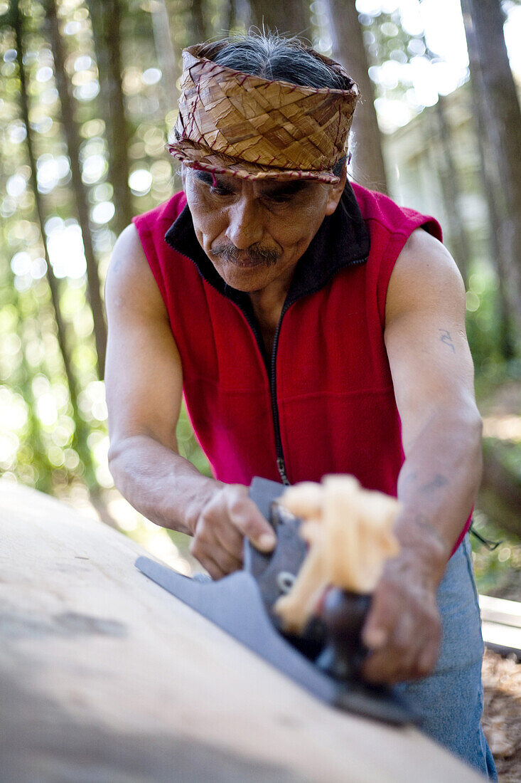 TOFINO, BRITISH COLUMBIA, CANADA. A man native to the West Coast of Vancouver Island carves a canoe as his tribes have for centuries.