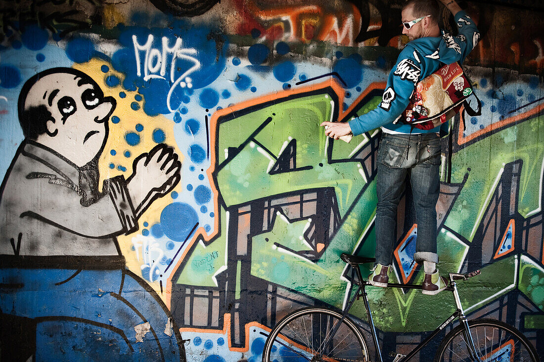 Sean Quigley standing on his fixed gear bicycle pretending to paint as a graffiti painted man preys for him.