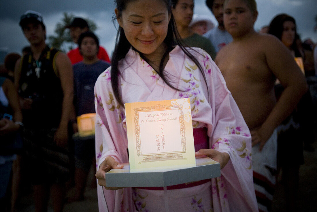 An Asian woman smiles as she looks down at her lantern while waiting to participate in the Lantern Floating Hawaii Ceremony on May 25th, 2009 at Magic Island in Honolulu, Hawaii. The ceremony is an Asian spiritual tradition that symbolizes the wish for al