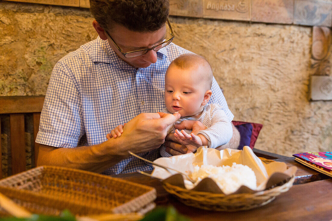Vater und Tochter essen im Restaurant, Baby probiert seinen ersten Reis, 5 Monate alt, Reiskorn, balinesisches Essen, Restaurant Biah Biah, Elternzeit in Asien, Europäer, Deutsche, Westler, Familie, MR, Ubud, Bali, Indonesien