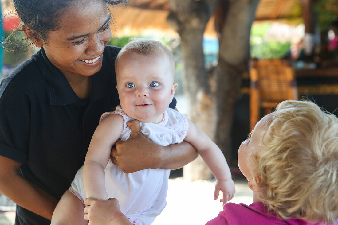 Balinese women holding German baby, laughing, smile, fond of children, intercultural contact, meeting local people, girl 5 months, boy 3 years old, family travel in Asia, parental leave, German, European, MR, Gili Air, Gili Inseln, Lombok, Indonesia