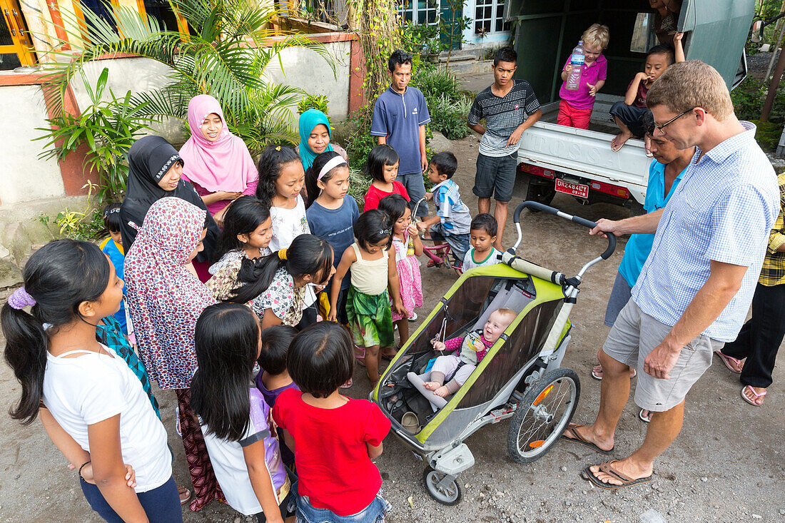 Indonesian villagers looking at little German baby, 5 months old, stroller, father, women and kids, children, Islam, head scarf, head rag, countryside, village, contact with local people, intercultural, family travel in Asia, parental leave, German, Europ
