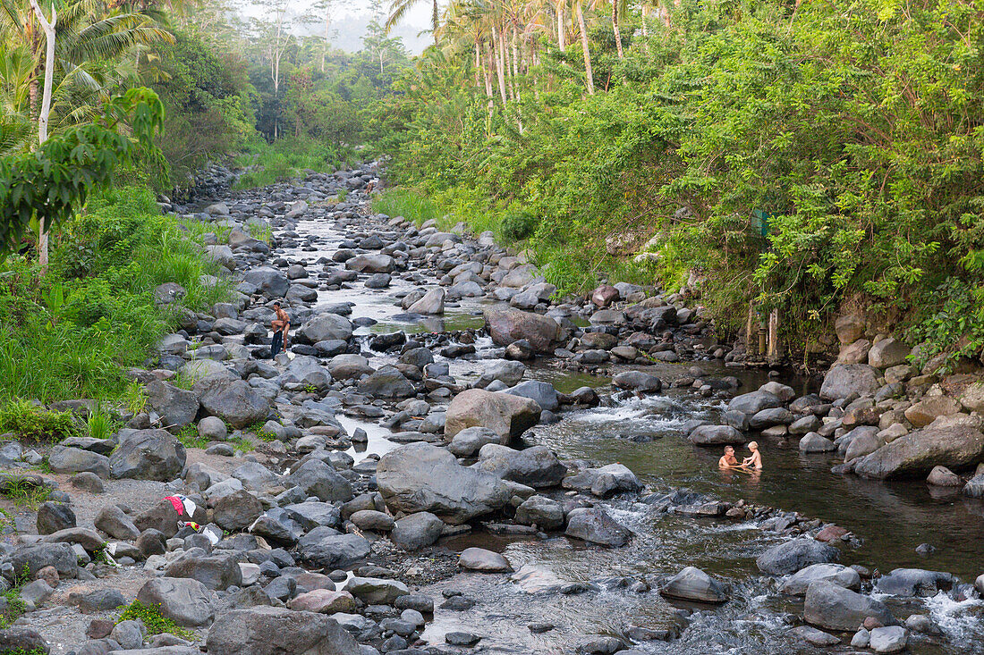 Father and son taking a bath in a river, riverbed, rocks, stones, local Balinese taking baths here, trees, local custom, intercultural, boy 3 years old, family on holiday, family travel in Asia, parental leave, Sidemen, Bali, Indonesia
