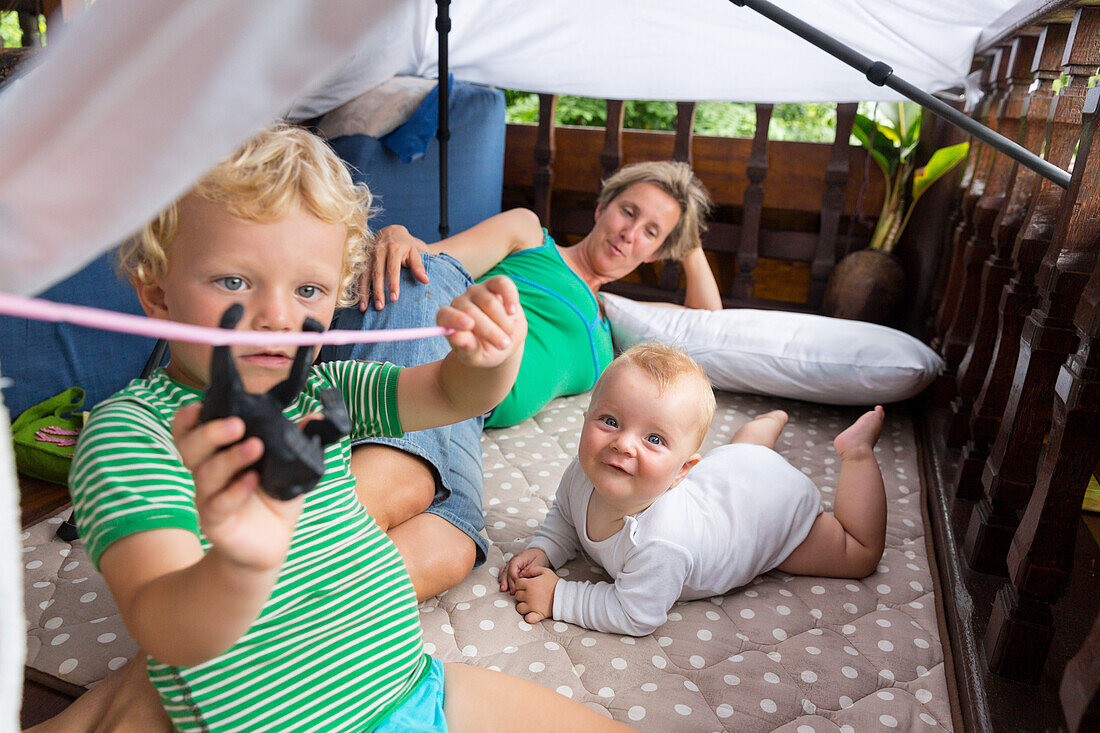 Familie im Urlaub, spielen, Junge, 3 Jahre spielt mit Affe, Strick, Baby, 5 Monate, Mädchen, lacht, Mama liegt auf Matte, Bude bauen, balinesische Ferienanlage, Hotel, Elternzeit in Asien, Europäer, Deutsche, Westler, Familie, MR, Sidemen, Bali, Indonesie