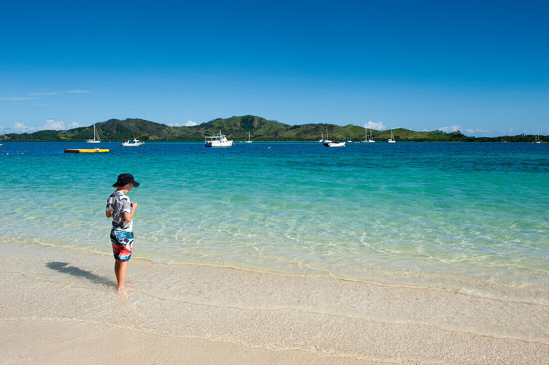 Eine Frau steht im Wasser am Strand mit Booten dahinter, Insel Malolo Lailai, Mamanuca-Inseln, Fidschi-Inseln, Südpazifik