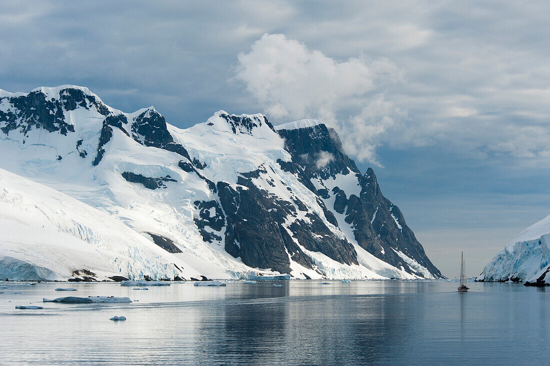 A sailing boat and snow-covered mountains, Lemaire Channel, near Graham Land Antarctica