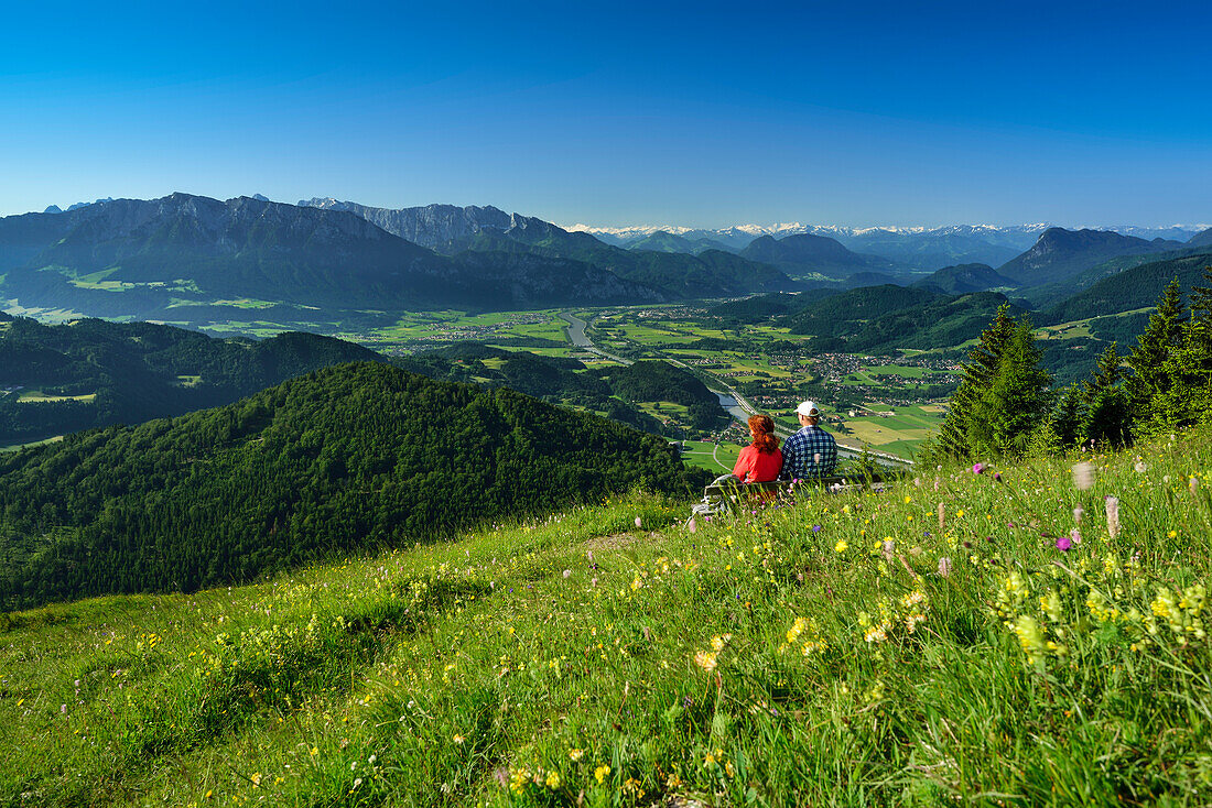 Two persons sitting on a bench in flower meadow, Inn valley in background, Kranzhorn, Chiemgau Alps, Tyrol, Austria