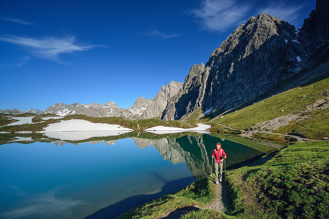 Woman hiking along lake Steinsee, Steinkarspitze and Schneekarlespitze in background, Lechtal Alps, Tyrol, Austria